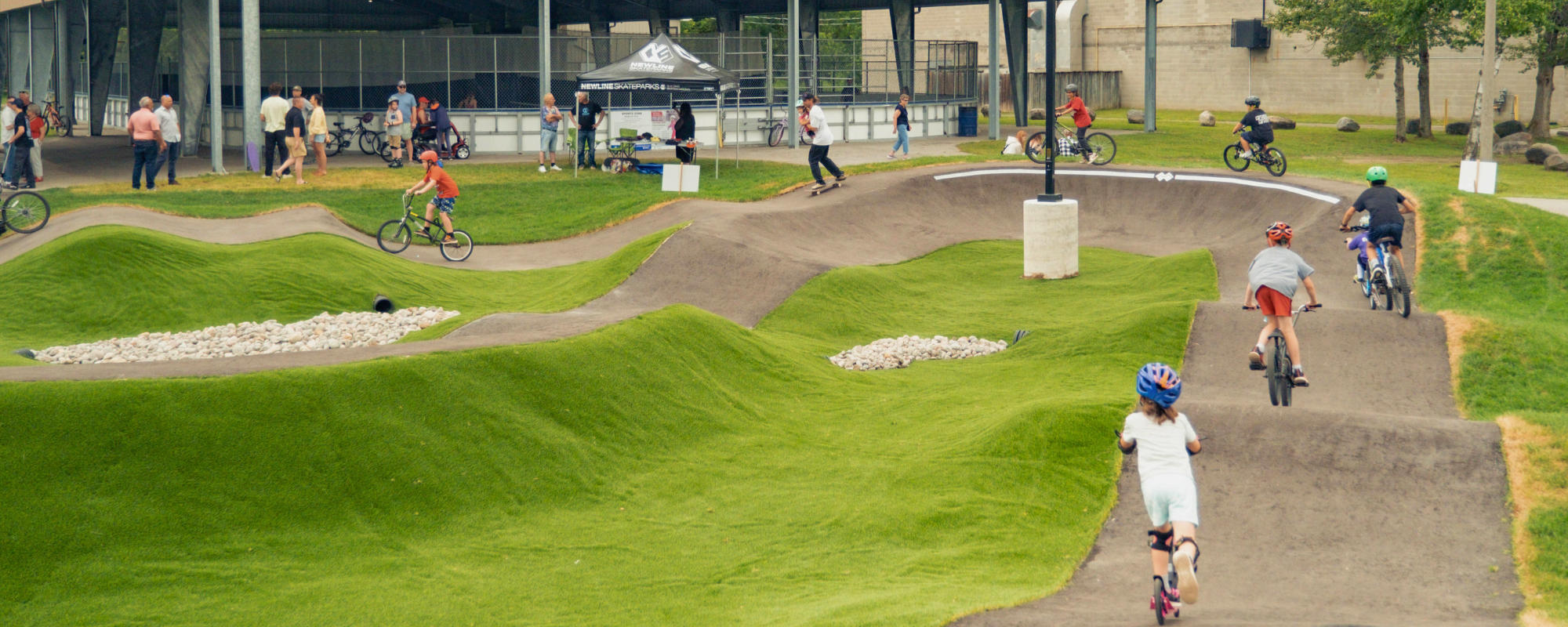 children on bikes and scooters on a concrete pump track with hills