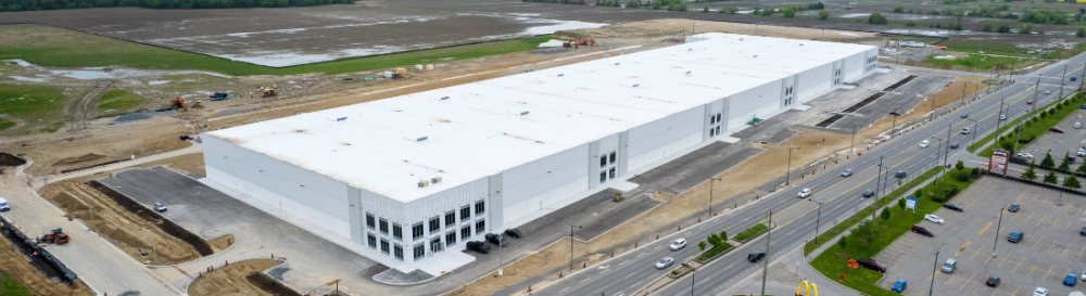 Aerial view of a large industrial building under construction beside a multi-lane road.